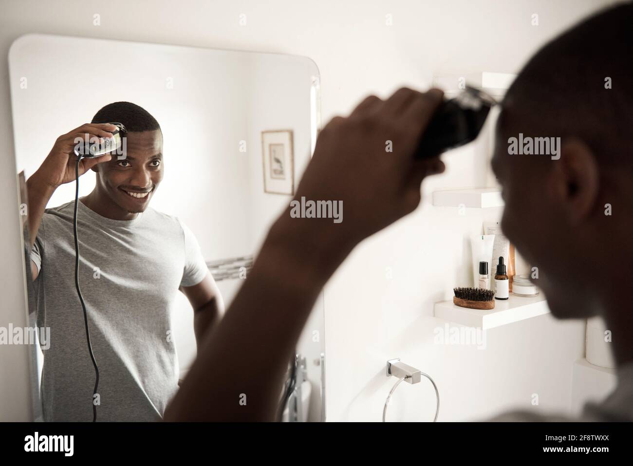 Sorridente uomo africano che rifilava i capelli nello specchio del bagno Foto Stock