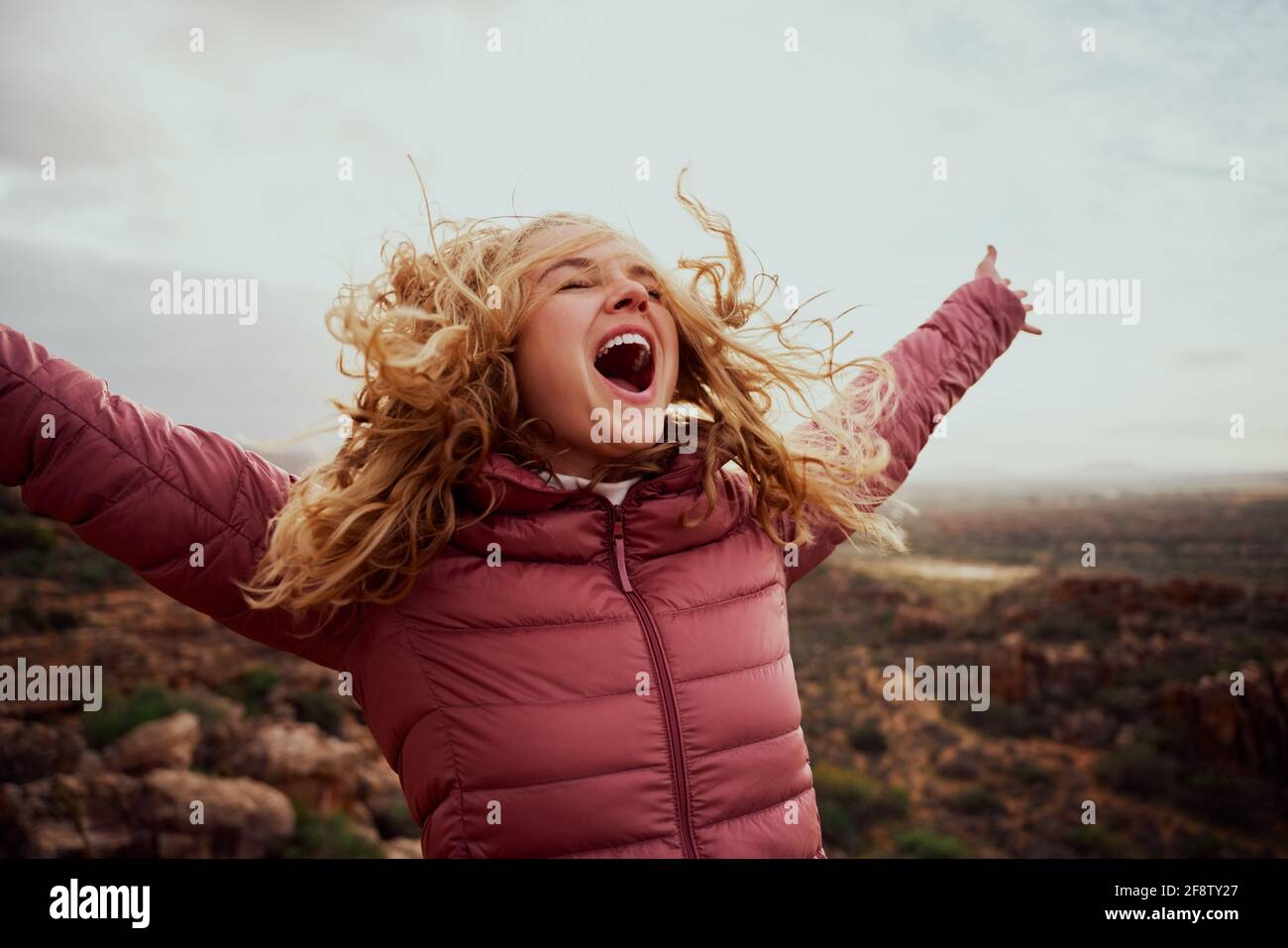 Primo piano di una bella donna sul sentiero di montagna con lei capelli volanti e mani allungate con bocca aperta Foto Stock