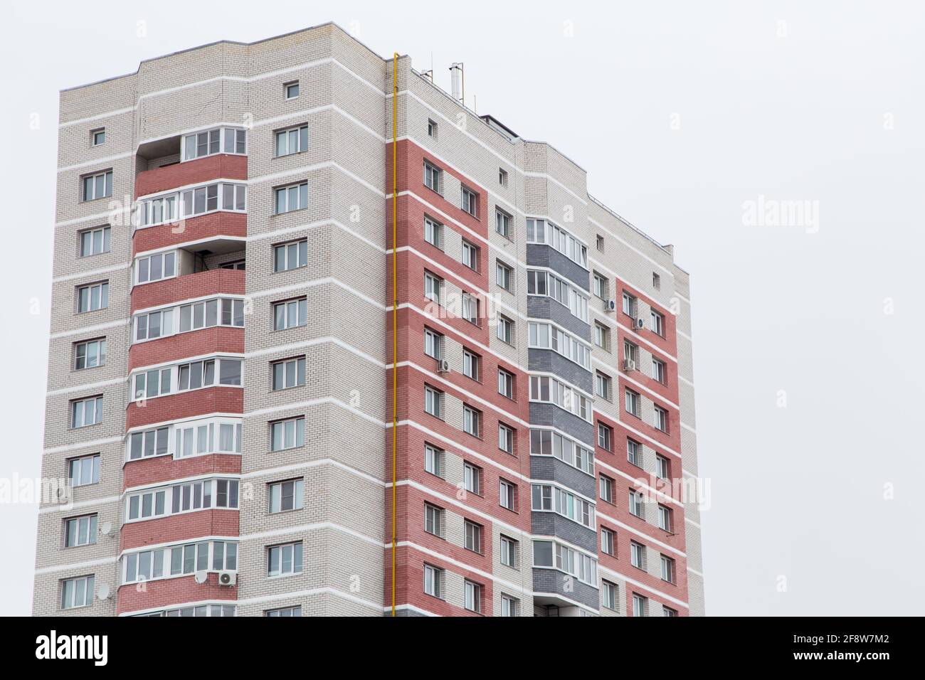 Alto edificio residenziale con balconi in mattoni rossi. Sullo sfondo del cielo grigio. Edifici nuovi e moderni, facciate degli edifici. Concetto di architettura immobiliare e urbana. Foto Stock