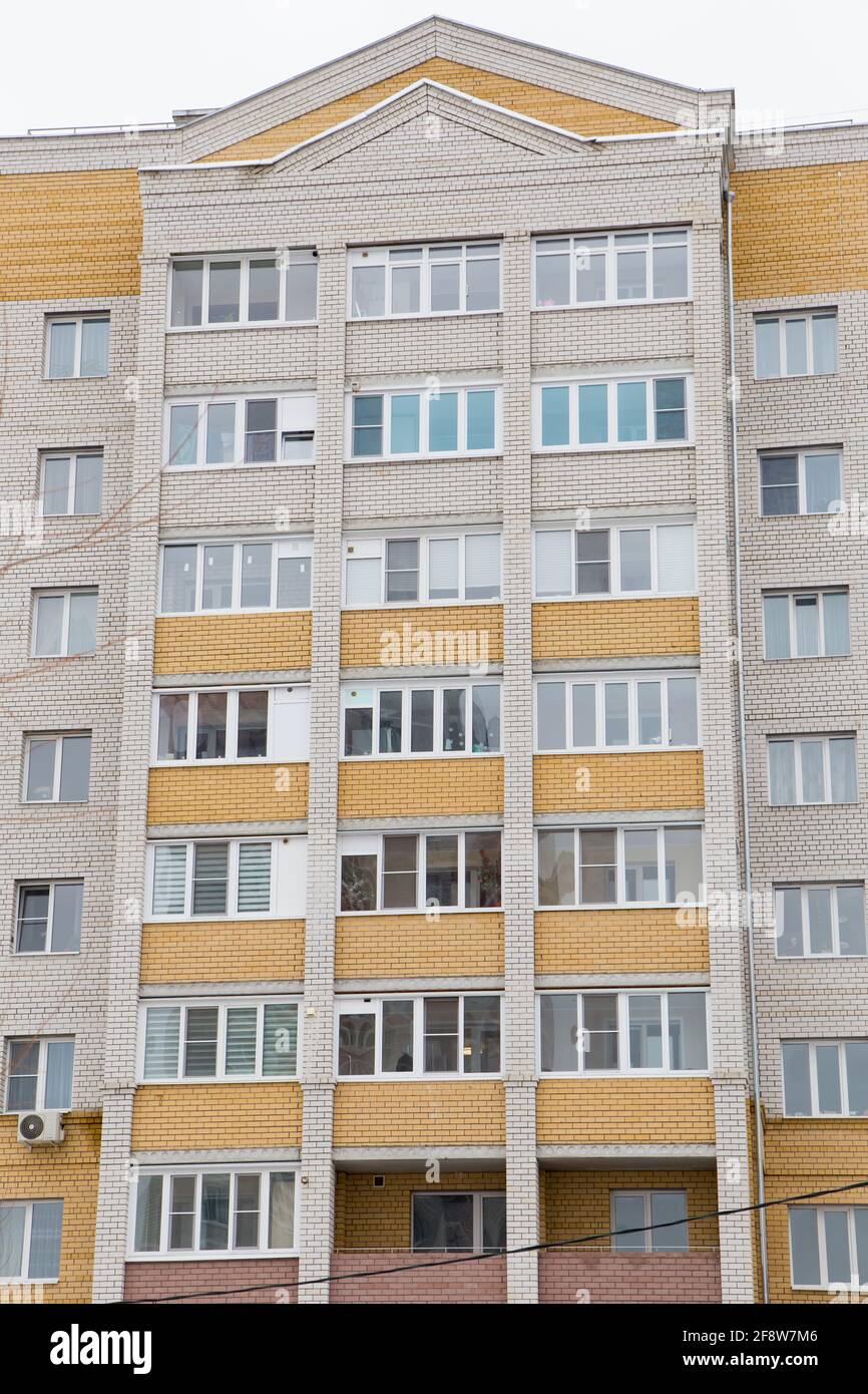 La facciata di un alto edificio in mattoni in un'area residenziale della citta'. Sullo sfondo del cielo grigio. Edifici nuovi e moderni, facciate degli edifici. Concetto di architettura immobiliare e urbana. Foto Stock