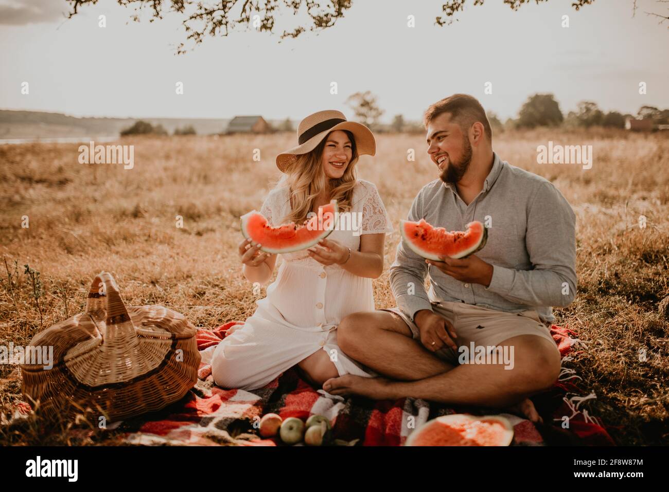 Felice famiglia europea caucasica con una donna incinta rilassarsi nella natura pic-nic mangiare frutta rosso succosa anguria ridere divertirsi Foto Stock