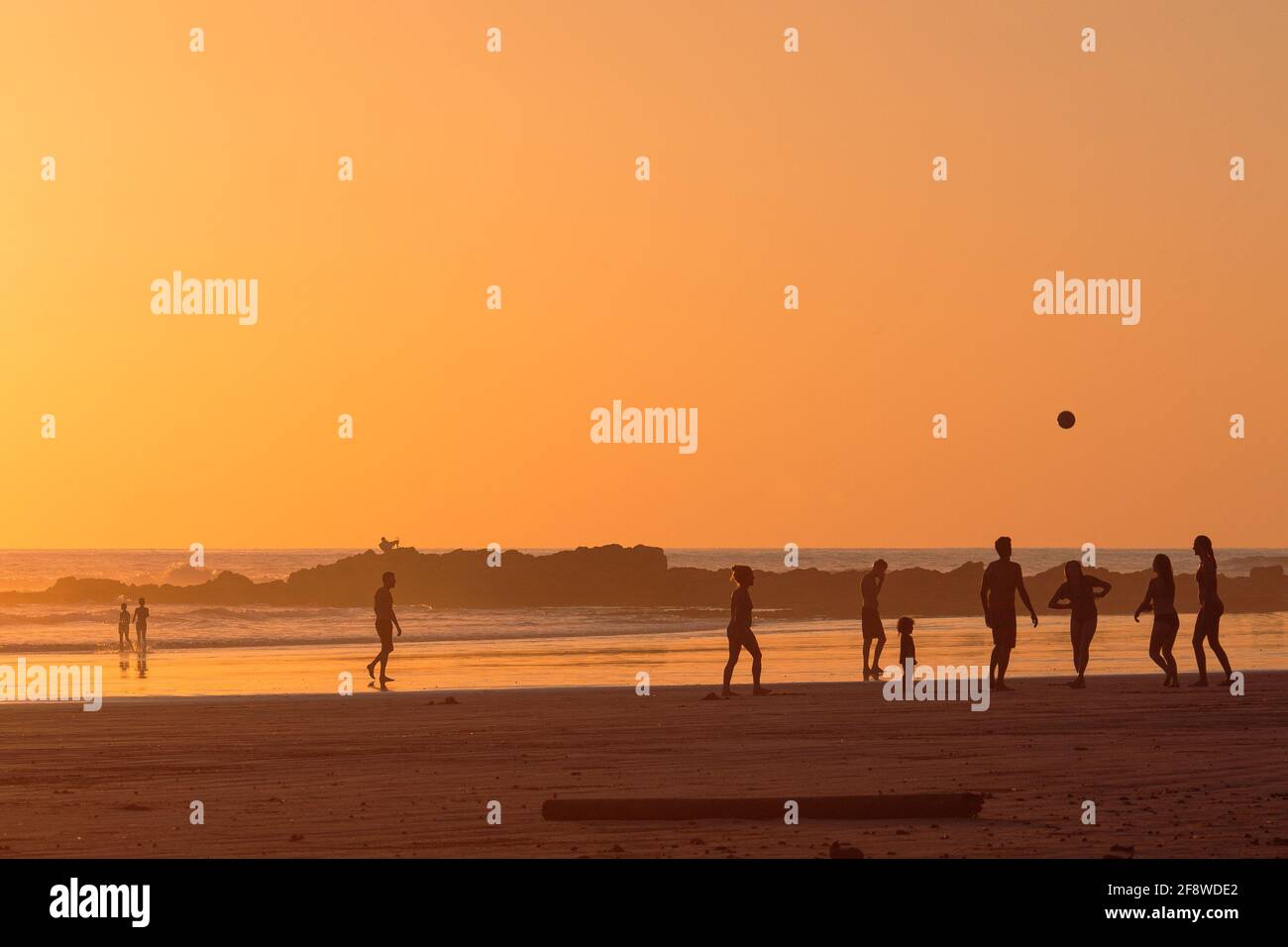 Famiglia e amici che giocano sulla spiaggia al tramonto Foto Stock