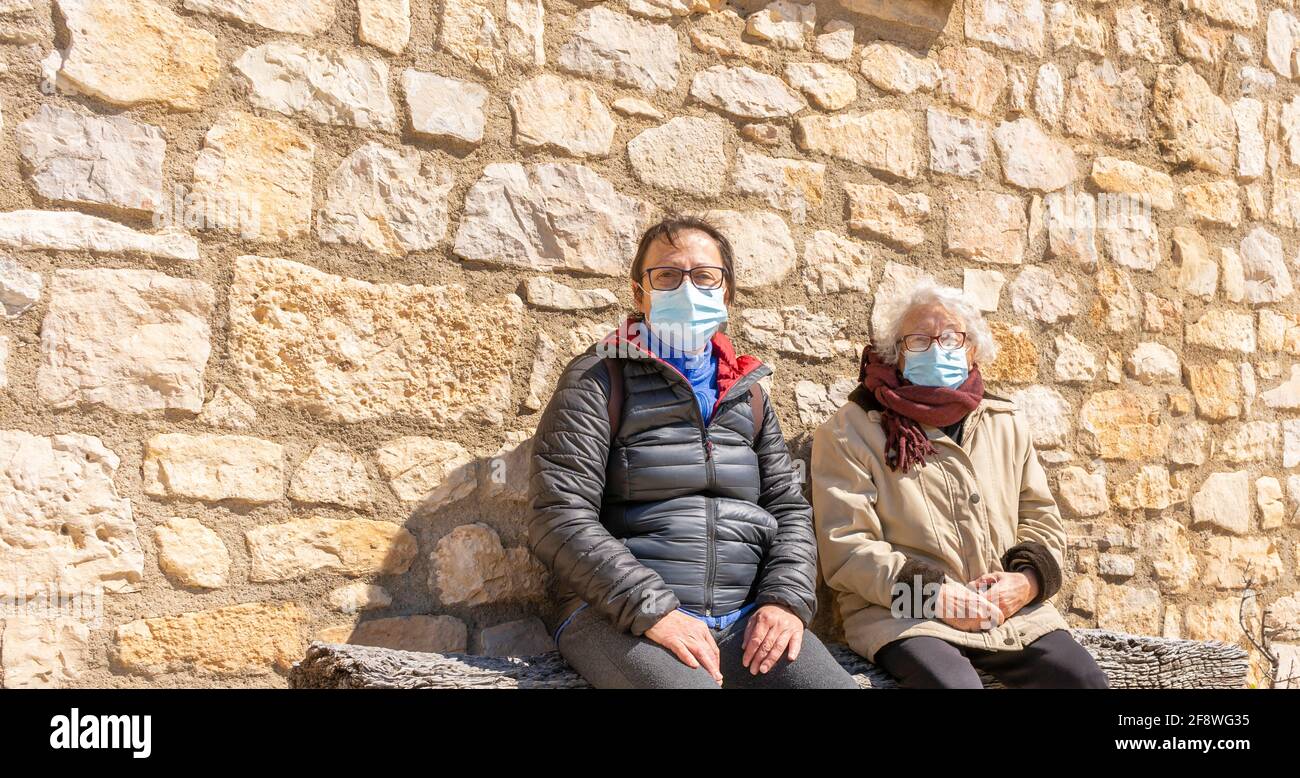 Donna anziana seduta con figlia che indossa una maschera protettiva durante la pandemia del coronavirus. Foto Stock