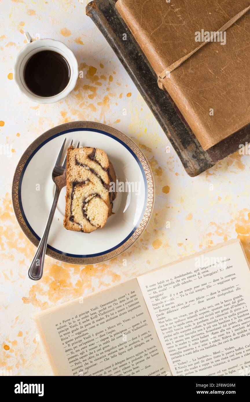 Un pezzo di babka in un piatto bianco con una forcella in acciaio. Sfondo bianco. Un libro aperto sulla destra e due vecchi libri sulla parte superiore. Una tazza di caffè. Foto Stock