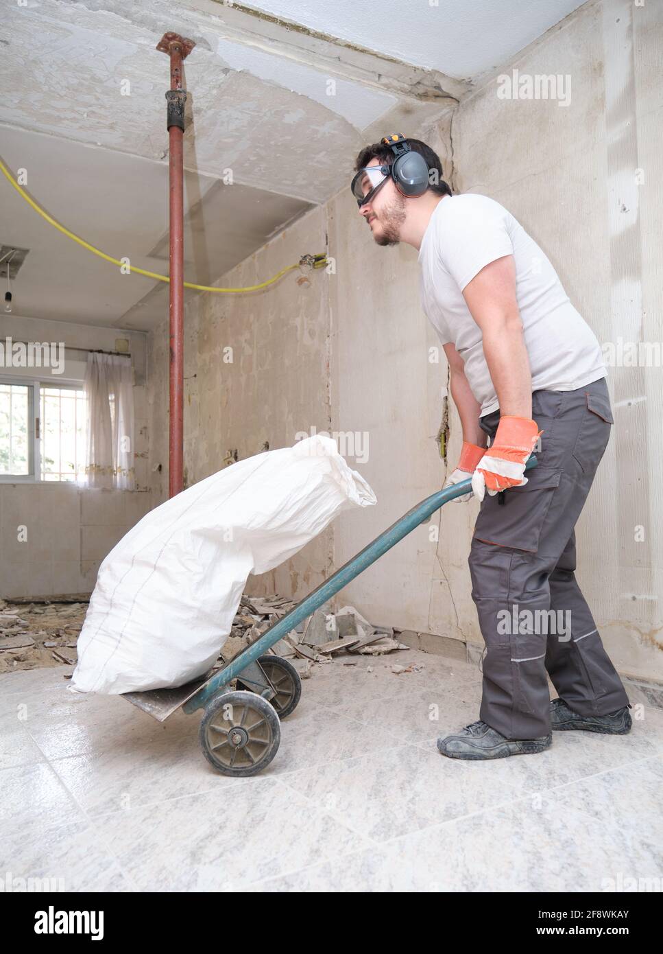 Costruttore che raccoglie i detriti da costruzione in un sacchetto e trasporta in un carrello manuale. Ristrutturazione della casa. Foto Stock