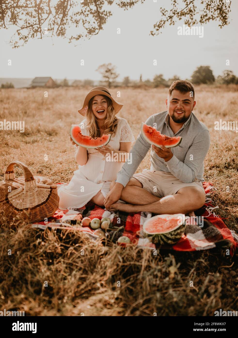 Felice famiglia europea caucasica con una donna incinta rilassarsi nella natura pic-nic mangiare frutta rosso succosa anguria ridere divertirsi Foto Stock