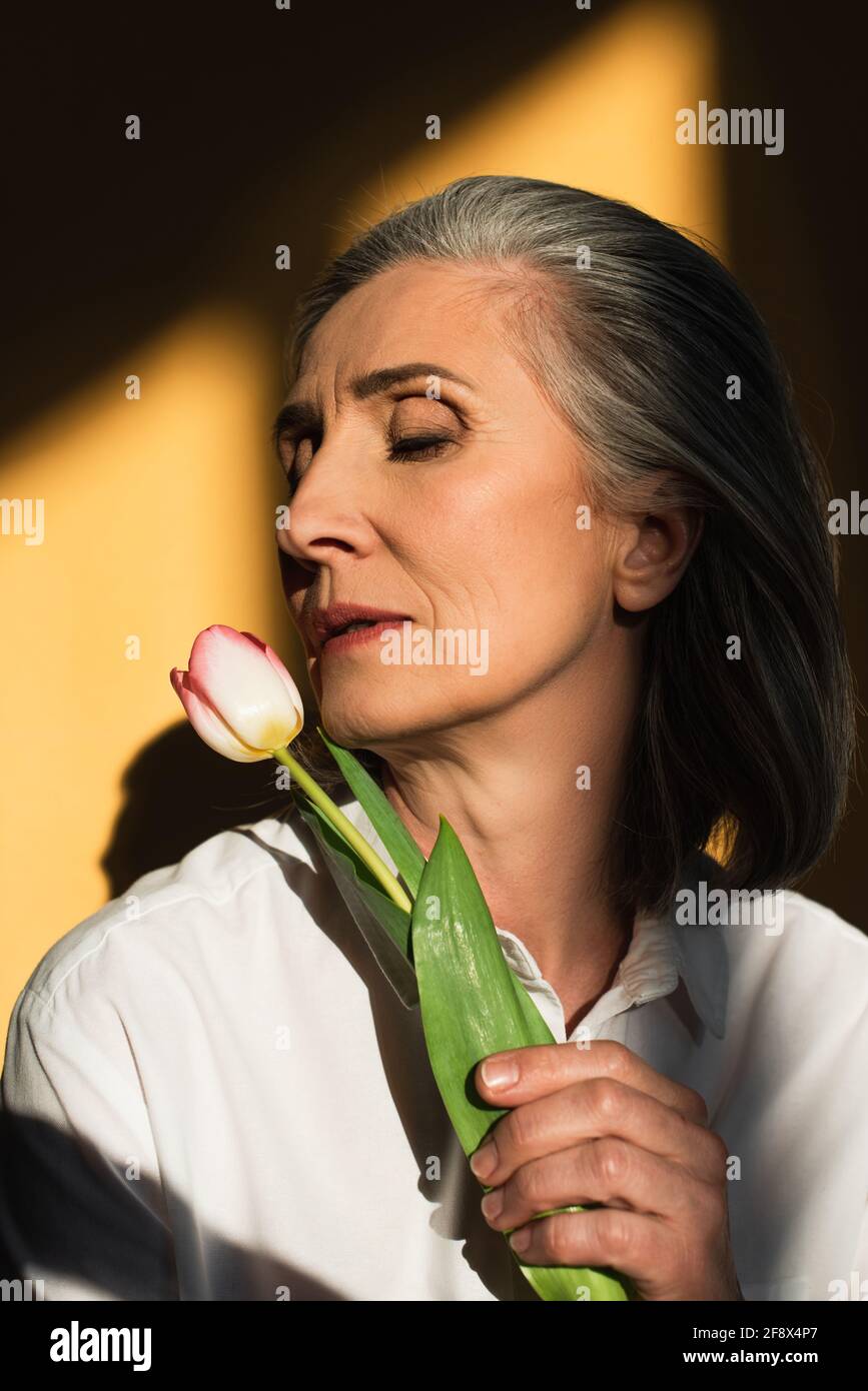 Donna matura in camicia bianca con tulipano su sfondo giallo con ombra Foto Stock