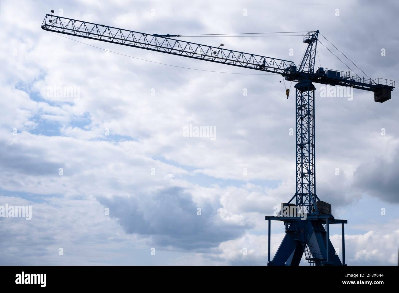 Silhouette di una gru a torre di costruzione alta contro il blu nuvoloso cielo alla fine della giornata Foto Stock