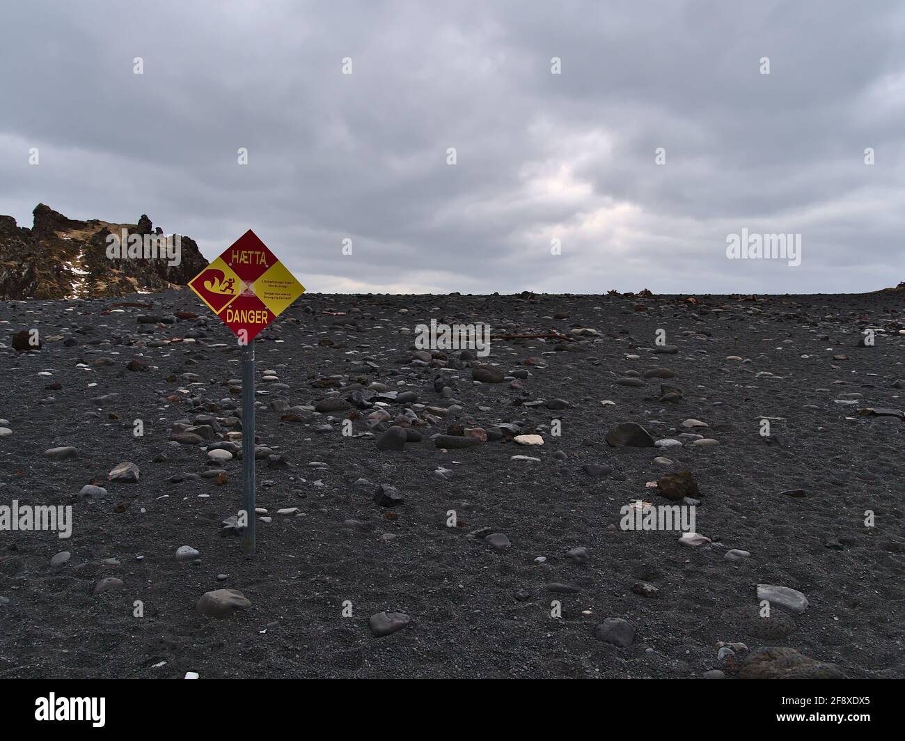 Vista della spiaggia Djupalonssandur sulla costa della penisola di Snaefellsnes con segno di avvertimento delle forti correnti sulla nuvolosa giornata invernale. Foto Stock