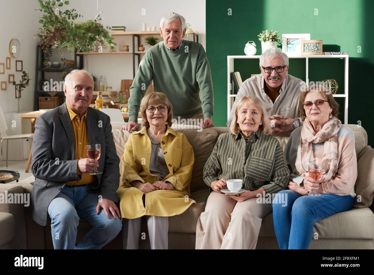 Ritratto di gruppo di vecchi amici seduti sul divano e. sorridendo alla macchina fotografica durante la riunione nella stanza Foto Stock