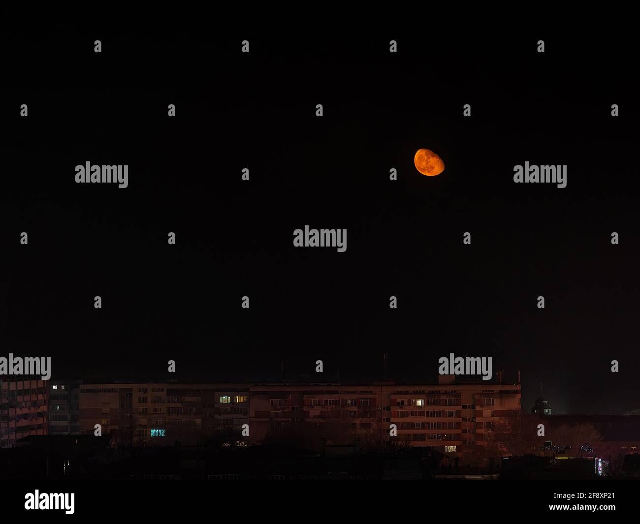 Si erge su edifici residenziali a più piani, con una grande luna arancione bassa nel cielo. Аstronomy, eclissi lunare, luna nella fase di Wanning Gibbous. Foto Stock