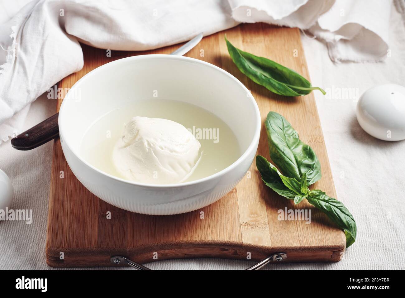 Palla di mozzarella in un recipiente e foglie di basilico fresco. Foto Stock