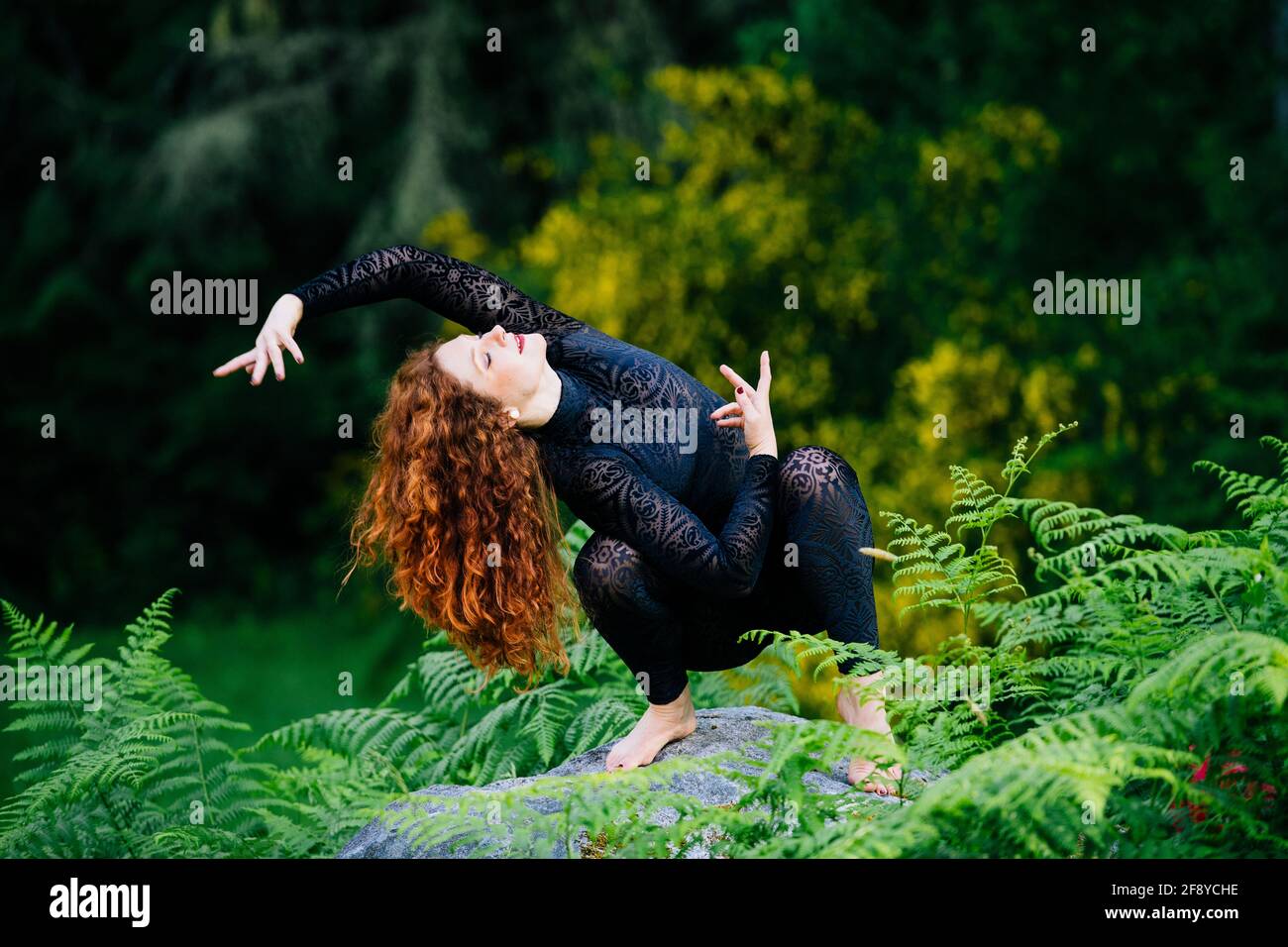 Donna Redhead che fa yoga sulla pietra nella foresta Foto Stock