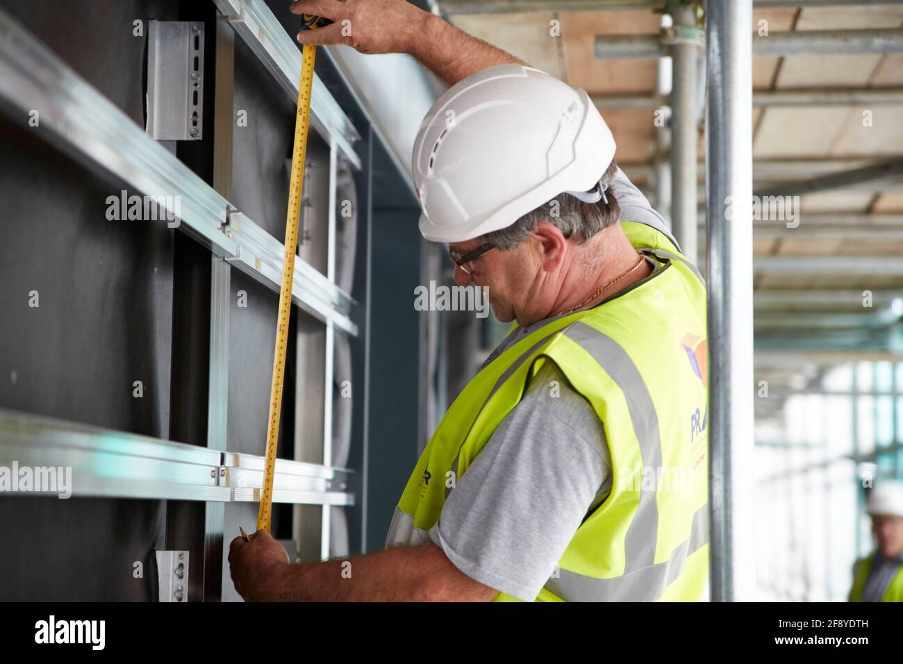 il lavoratore di costruzione sul cantiere misura i fissaggi per i rivestimenti Foto Stock