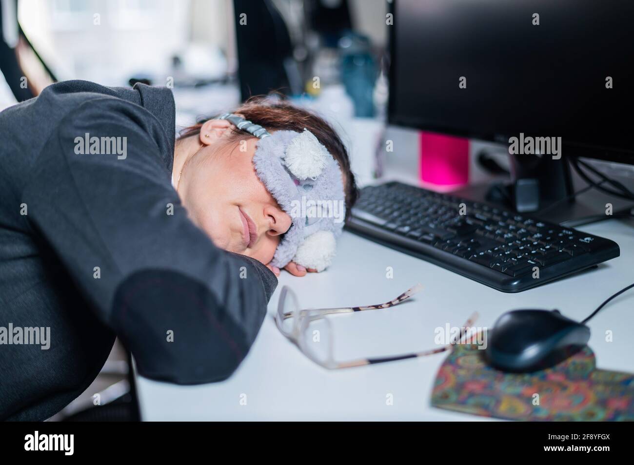 Donna d'affari in una maschera bendata addormentata in ufficio. Impiegato esausto sul posto di lavoro Foto Stock