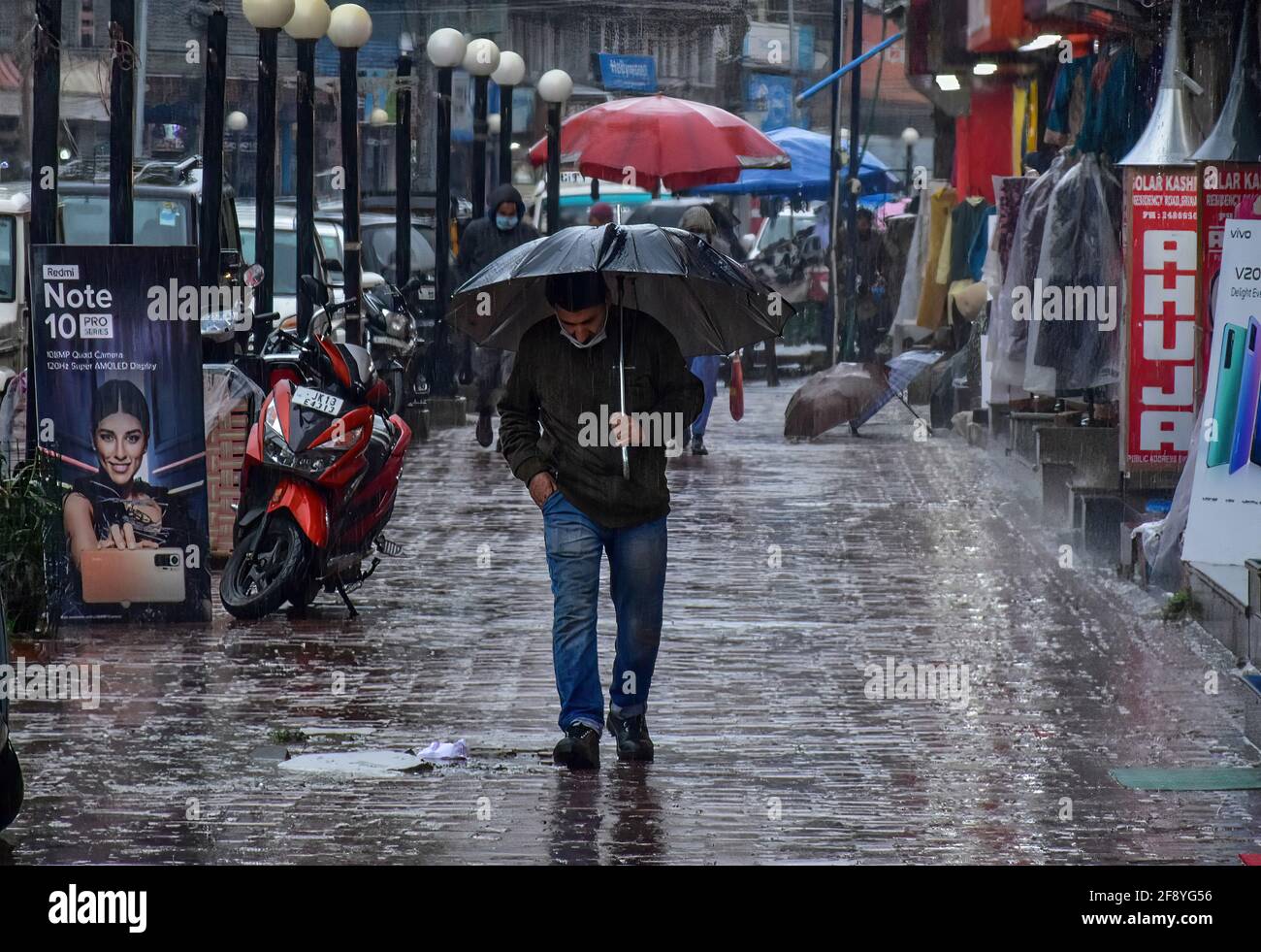 Srinagar, India. 15 Aprile 2021. Un uomo tiene un ombrello mentre cammina lungo una strada durante le precipitazioni a Srinagar. Credit: SOPA Images Limited/Alamy Live News Foto Stock