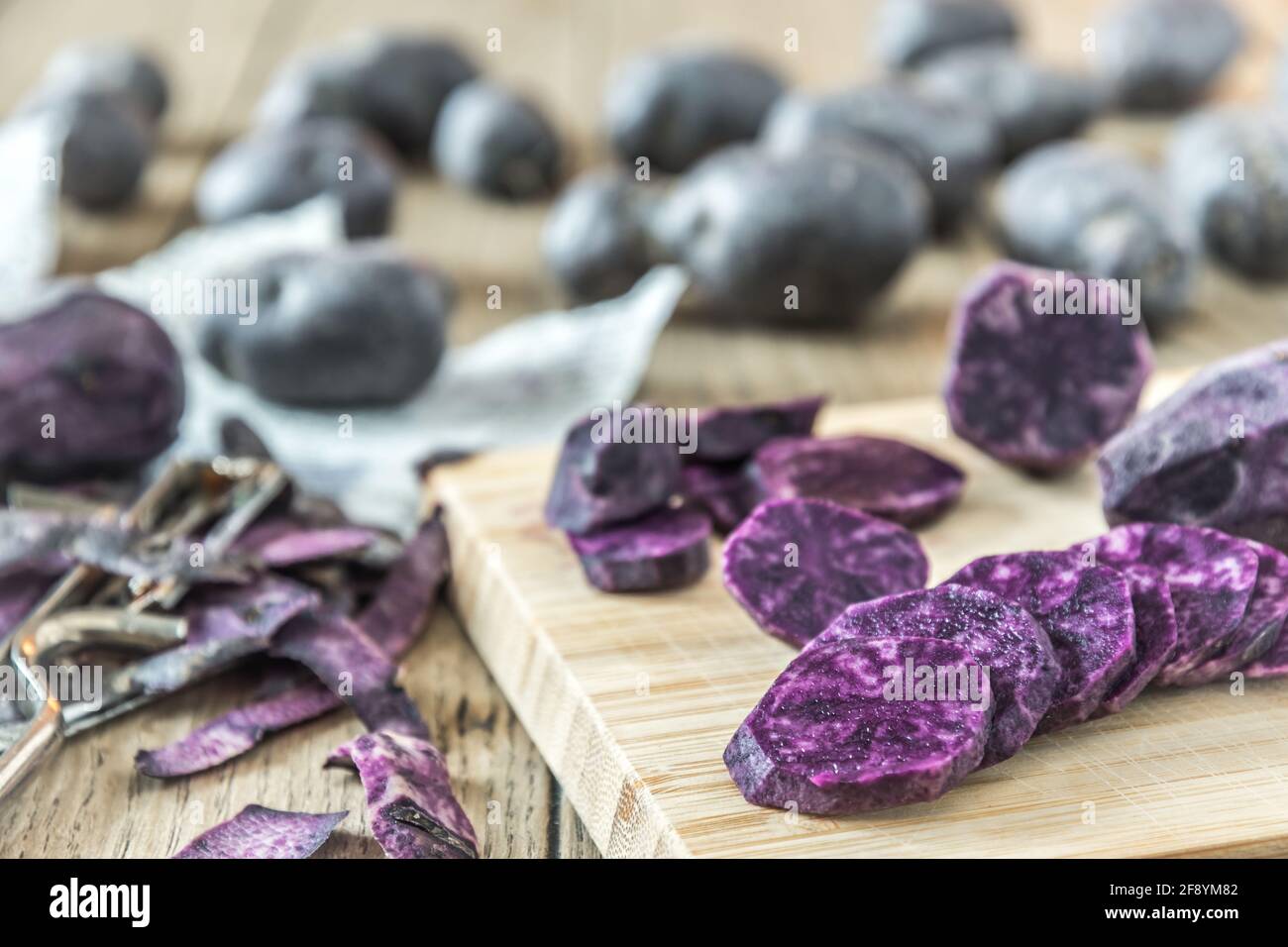 Patate porpora sbucciate e tagliate a fette su una tavola di legno, patate intere sullo sfondo Foto Stock