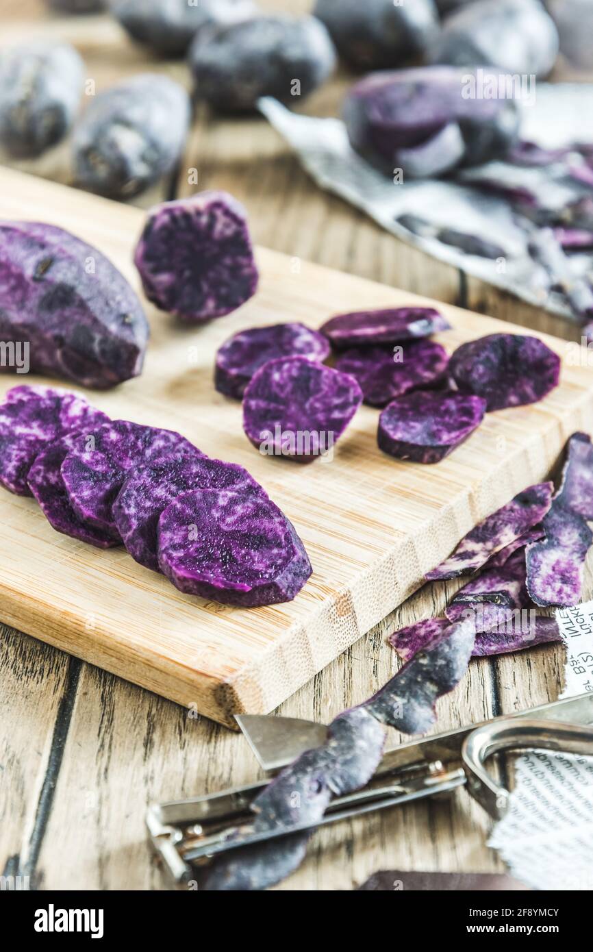 Patate viola sbucciate e tagliate a fette su tavola di legno, patate intere sullo sfondo, verticali Foto Stock