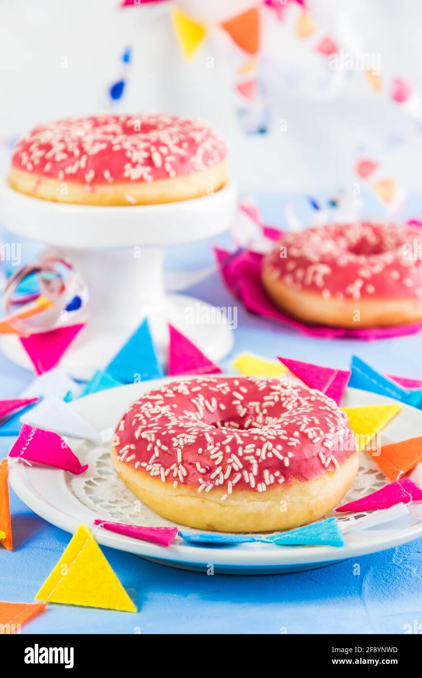 Ciambelle glassate rosa su sfondo azzurro, decorate con ruscelli e una ghirlanda di festa, concentrarsi sulla ciambella anteriore, verticale Foto Stock