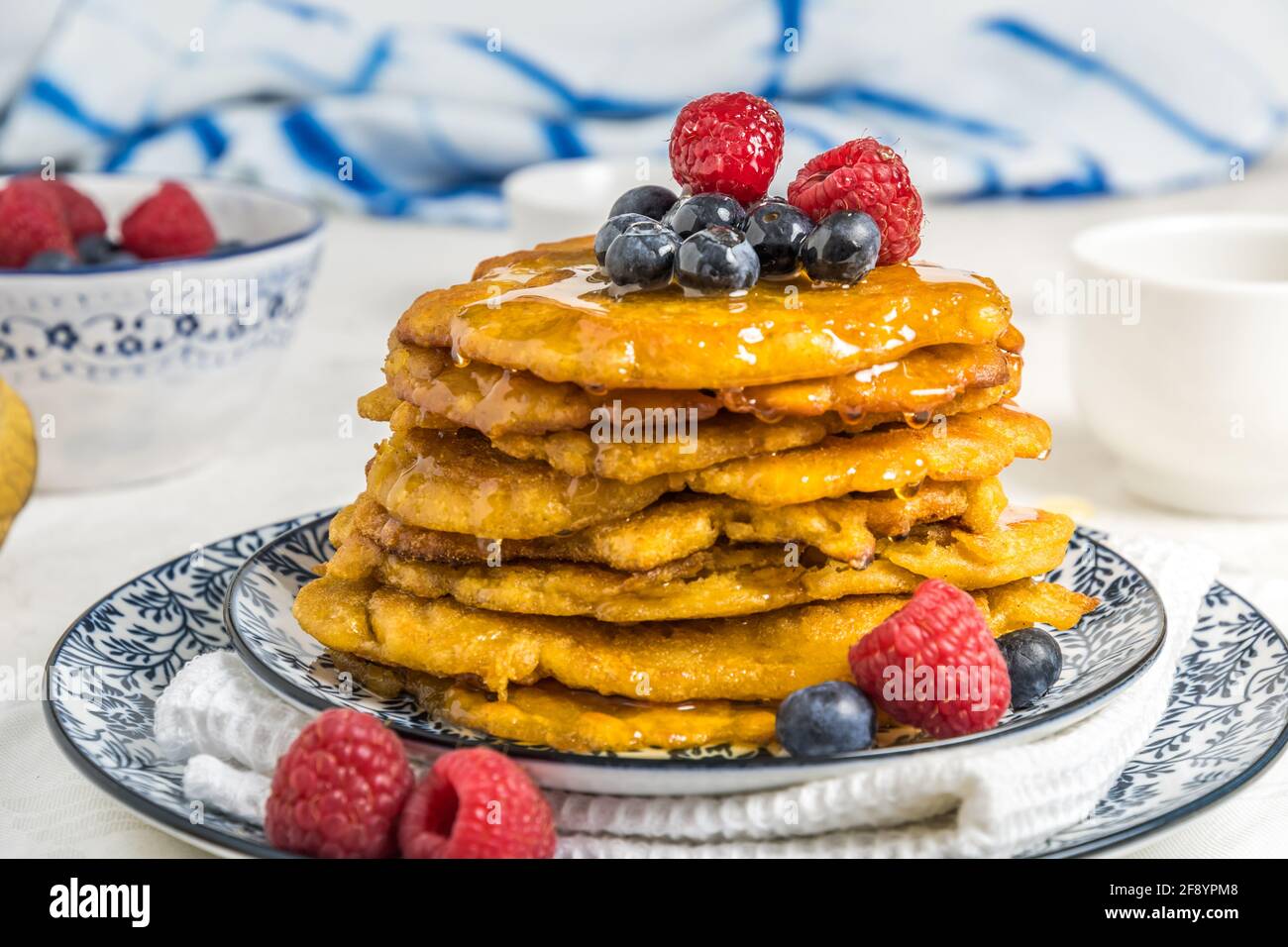 Pila di frittelle vegane con frutti di bosco e sciroppo su a. piastra con motivi blu-bianchi su sfondo bianco Foto Stock
