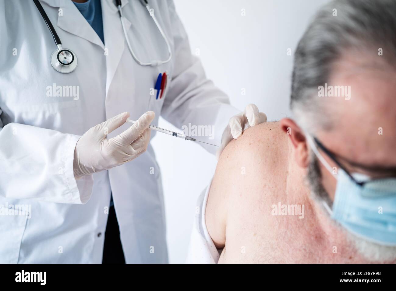 Primo piano di un medico che vaccina un uomo anziano con Una maschera chirurgica con il vaccino Covid-19 Foto Stock