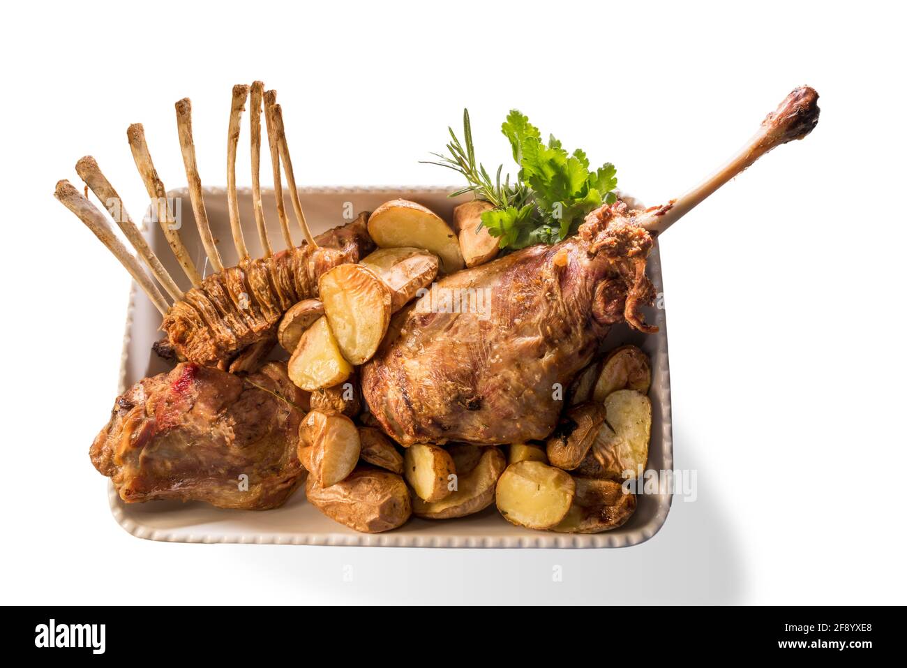 Coscia arrosto e costolette di agnello in vassoio di ceramica con patate e prezzemolo, isolato su bianco, vista dall'alto Foto Stock