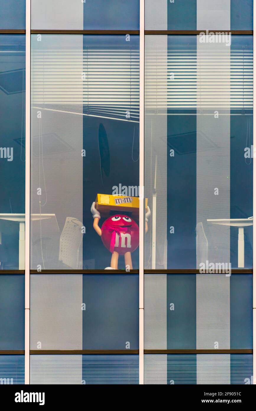 La grande figura rossa di M's da solo in un edificio vuoto durante la pandemia del virus corona. Questa è la mascotte di carattere del cioccolato marca m&m's prodotto Foto Stock