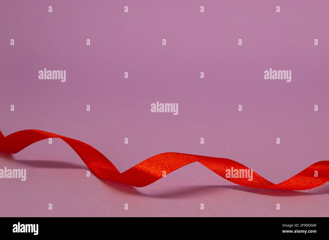 Il nastro rosso satinato ricci su sfondo lilla, spazio libero. Foto Stock