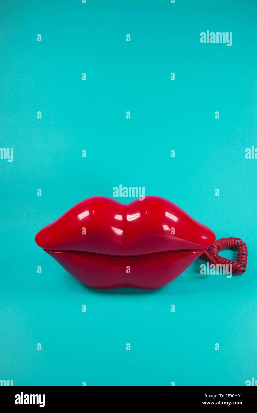 Vecchio telefono a forma di labbra rosse scure su uno sfondo blu tenue. Astratto minimo. San Valentino, amore, invio baci idea. In attesa di una chiamata tra Foto Stock