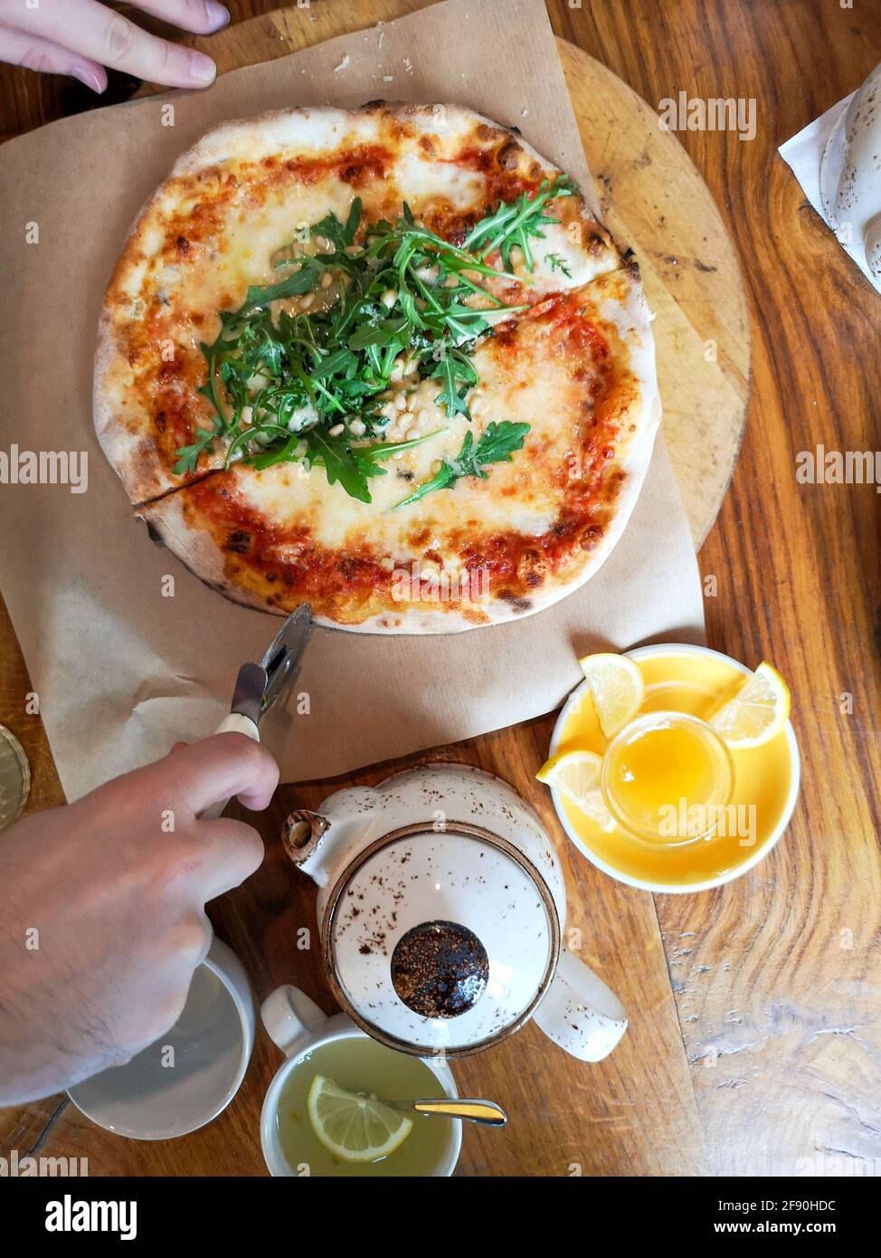 Mani di un uomo che taglia pizza, tè, limone su un tavolo di legno in un caffè Foto Stock