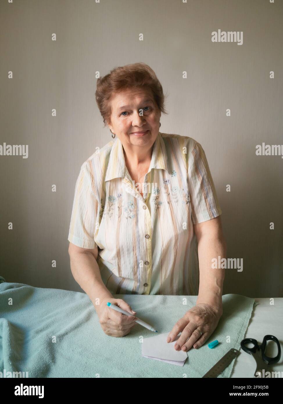 Una donna anziana fa un modello di maschera medica su un tessuto Foto Stock