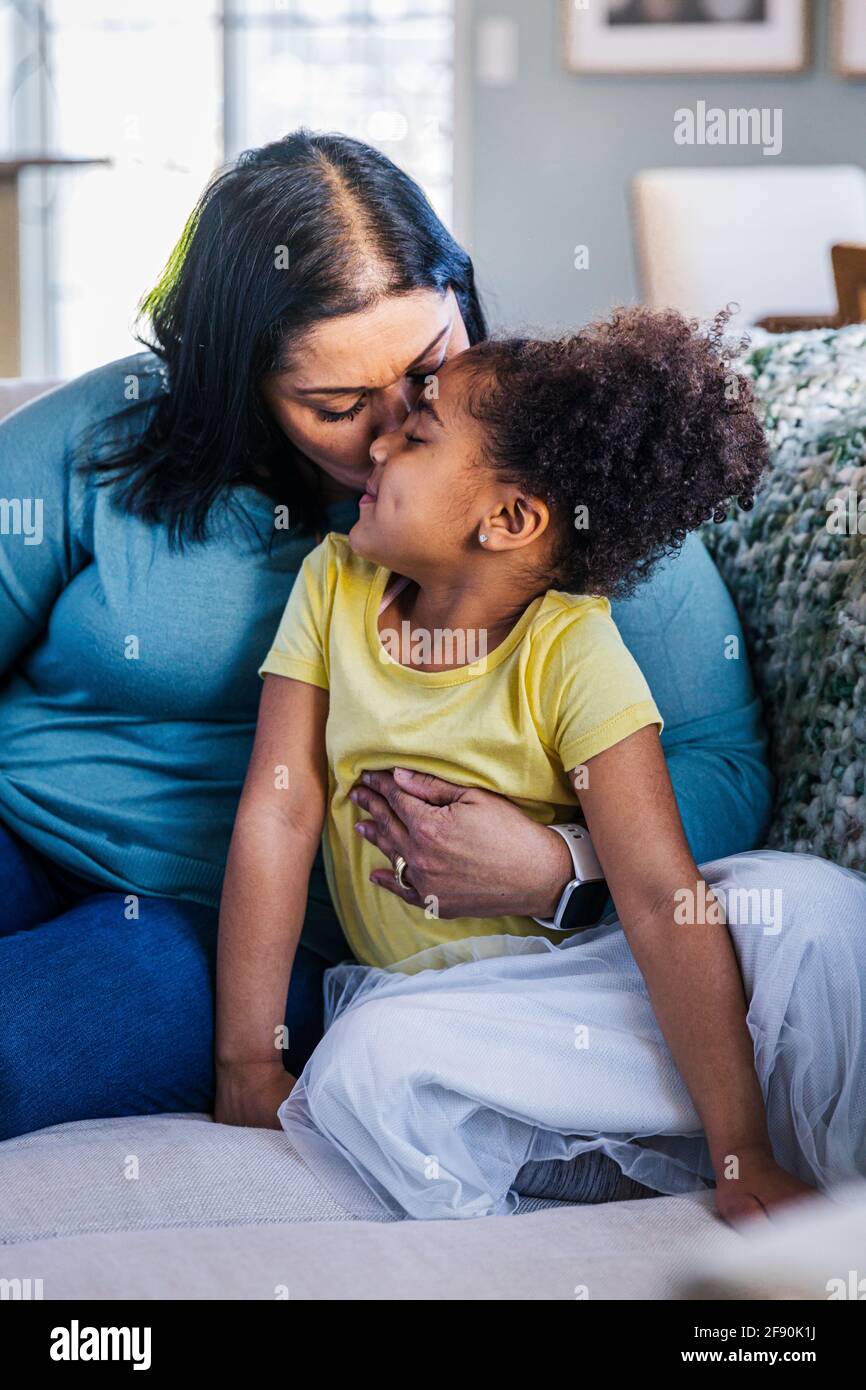 Nonna che bacia la nipote mentre si siede sul divano a casa Foto Stock