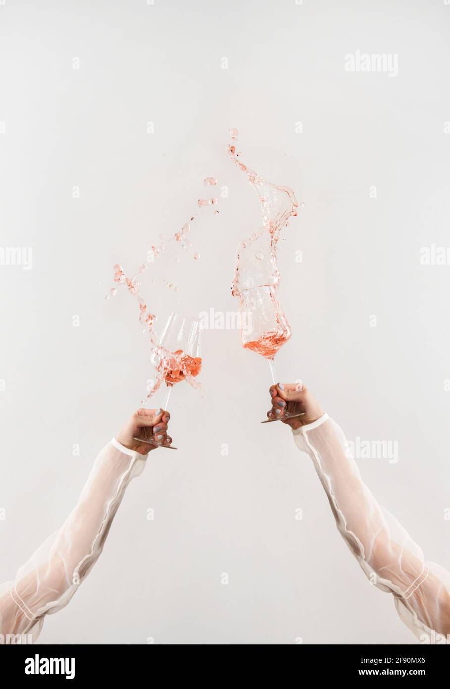 Mani femminili in eleganti camicie trasparenti bicchieri da versare con vino rosato fresco che vola in aria su fondo bianco. Degustazione di vini, vino s Foto Stock