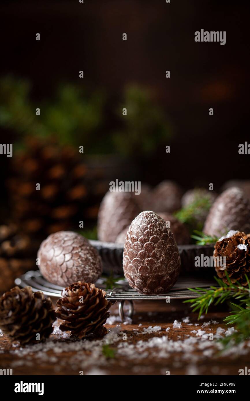 Cioccolatini festosi a forma di cono di pino su una rastrelliera metallica circondata da sprigs di abete e coni di pino reali Foto Stock