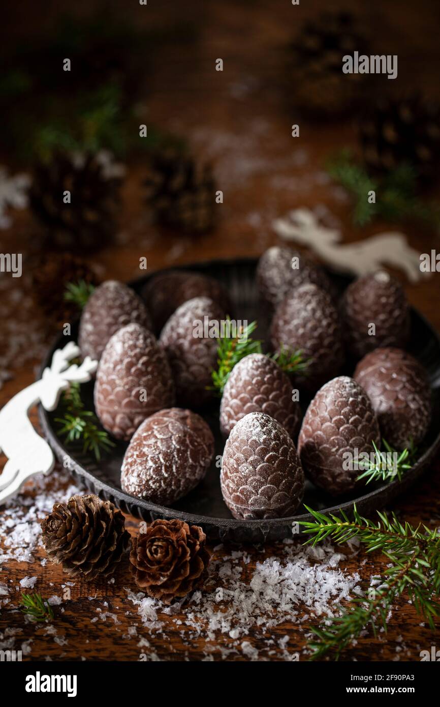 Cioccolatini a forma di cono di pino su un piatto di metallo circondato da molle di abete e coni di pino reali Foto Stock