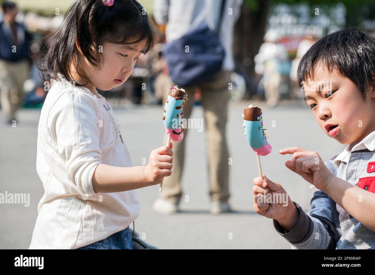 Due bambini giapponesi giovani - ragazzo e ragazza si dilettano nel mangiare gelato su un bastone, Tokyo, Giappone Foto Stock