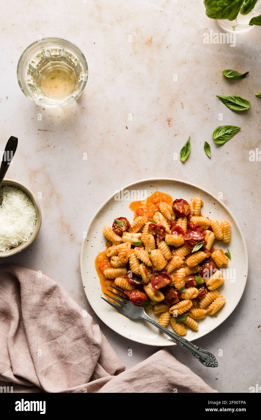 Piatto di cavatelli con pomodori ciliegini, piccola ciotola di parmigiano e bicchiere di vino. Foto Stock