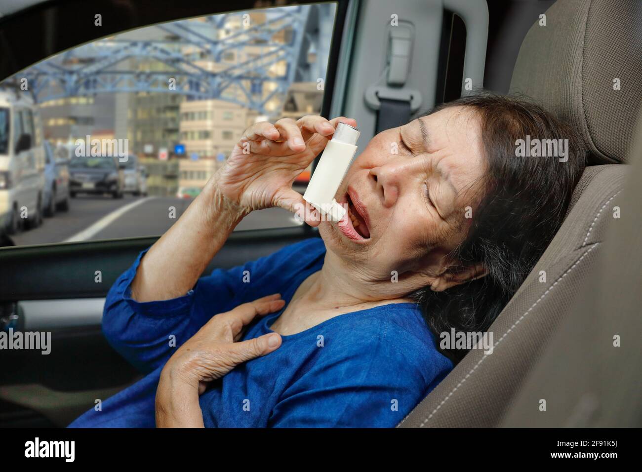 Donna anziana soffocante e che tiene uno spray per l'asma all'interno dell'auto sulla strada Foto Stock