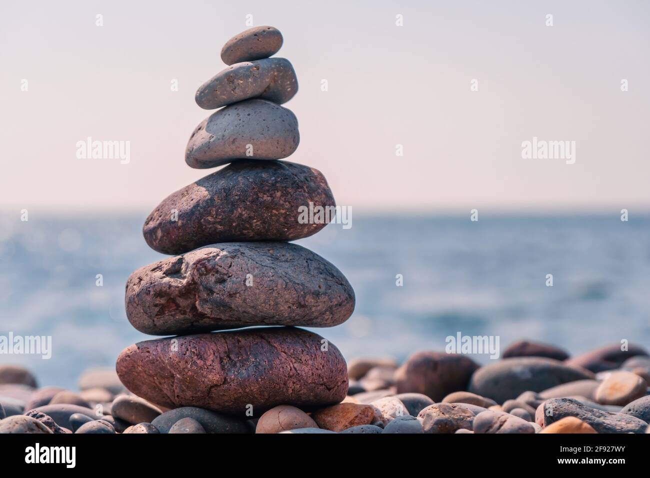 Equilibrata piramide di ciottoli sulla spiaggia in una giornata di sole. Abstract Sea bokeh sullo sfondo. Messa a fuoco selettiva. Pietre Zen sulla spiaggia di mare, meditazione Foto Stock