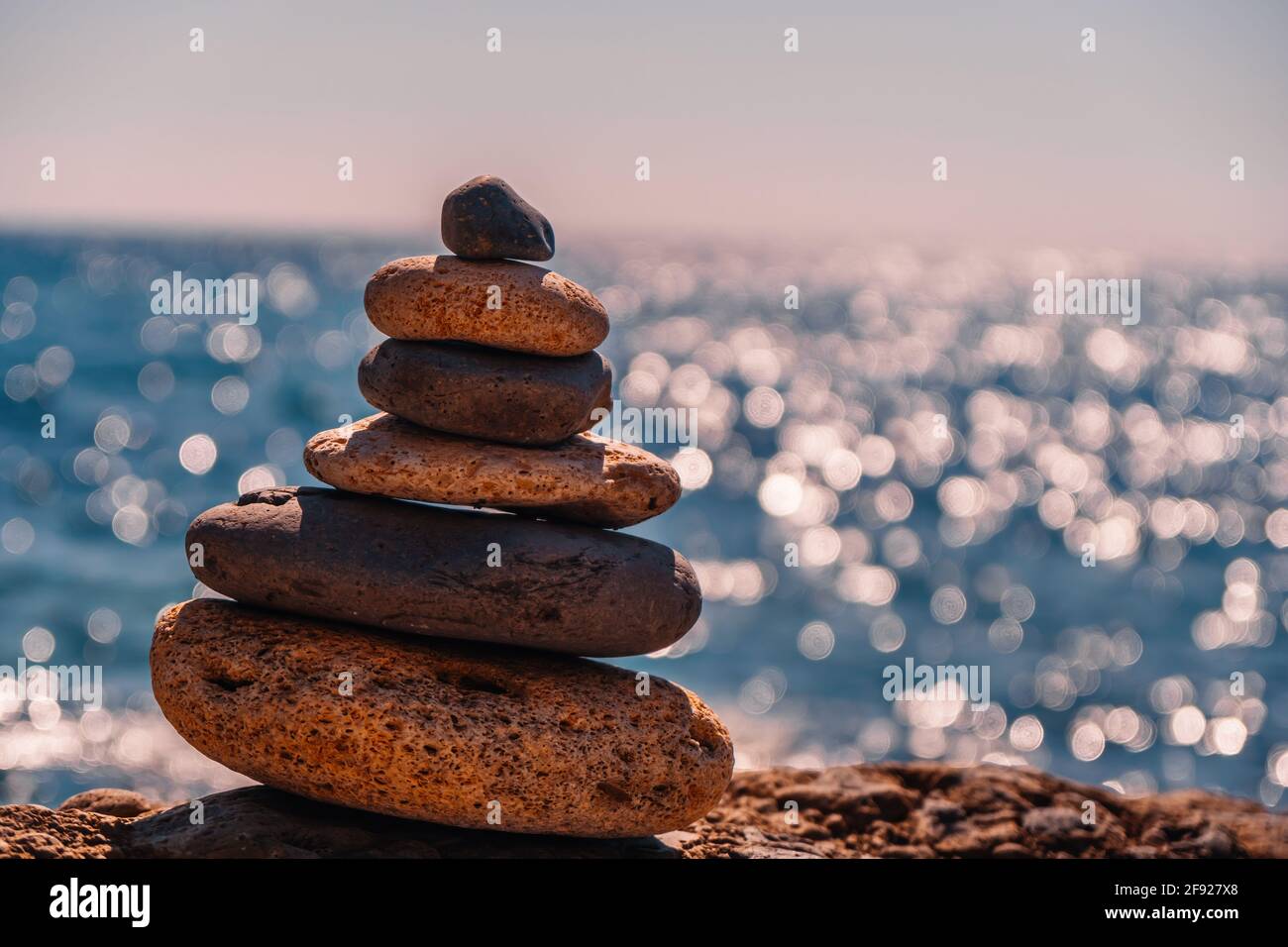 Equilibrata piramide di ciottoli sulla spiaggia in una giornata di sole. Abstract Sea bokeh sullo sfondo. Messa a fuoco selettiva. Pietre Zen sulla spiaggia di mare, meditazione Foto Stock
