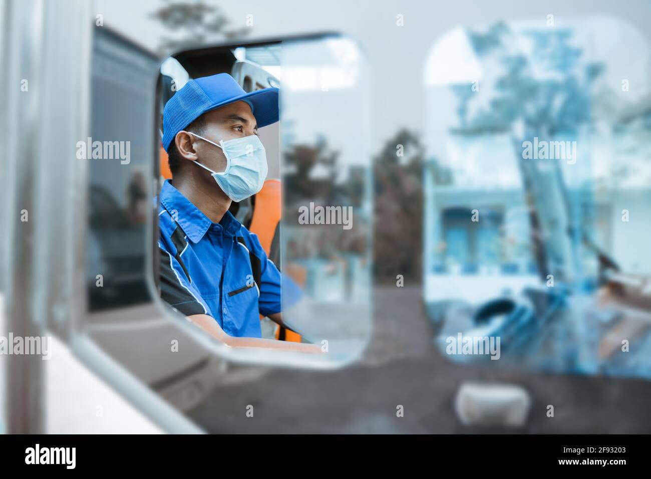visto dalla finestra di un driver maschio in una uniforme e indossare una maschera mentre si trova dietro la ruota Foto Stock