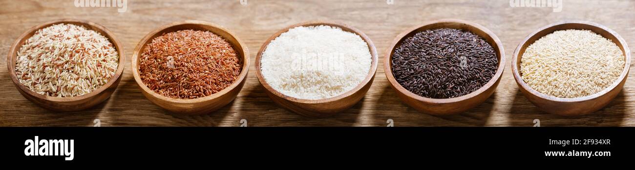 Vari tipi di riso: Bianco, marrone, grano misto, riso nero e rosso in una ciotola su fondo di legno Foto Stock