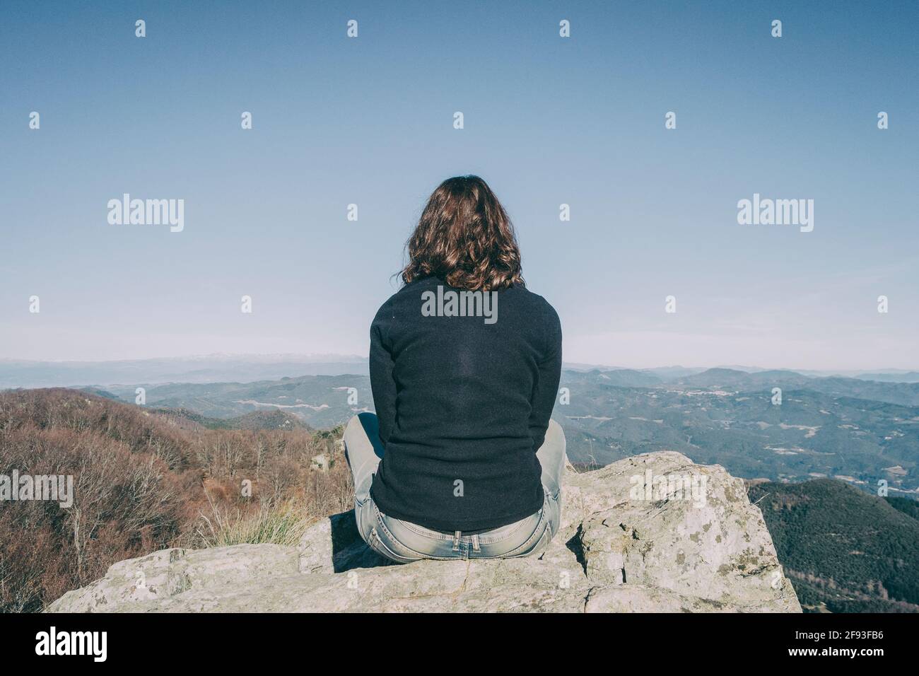 ragazza dalla parte posteriore seduta su una pietra superiore guardando alle montagne lontane Foto Stock