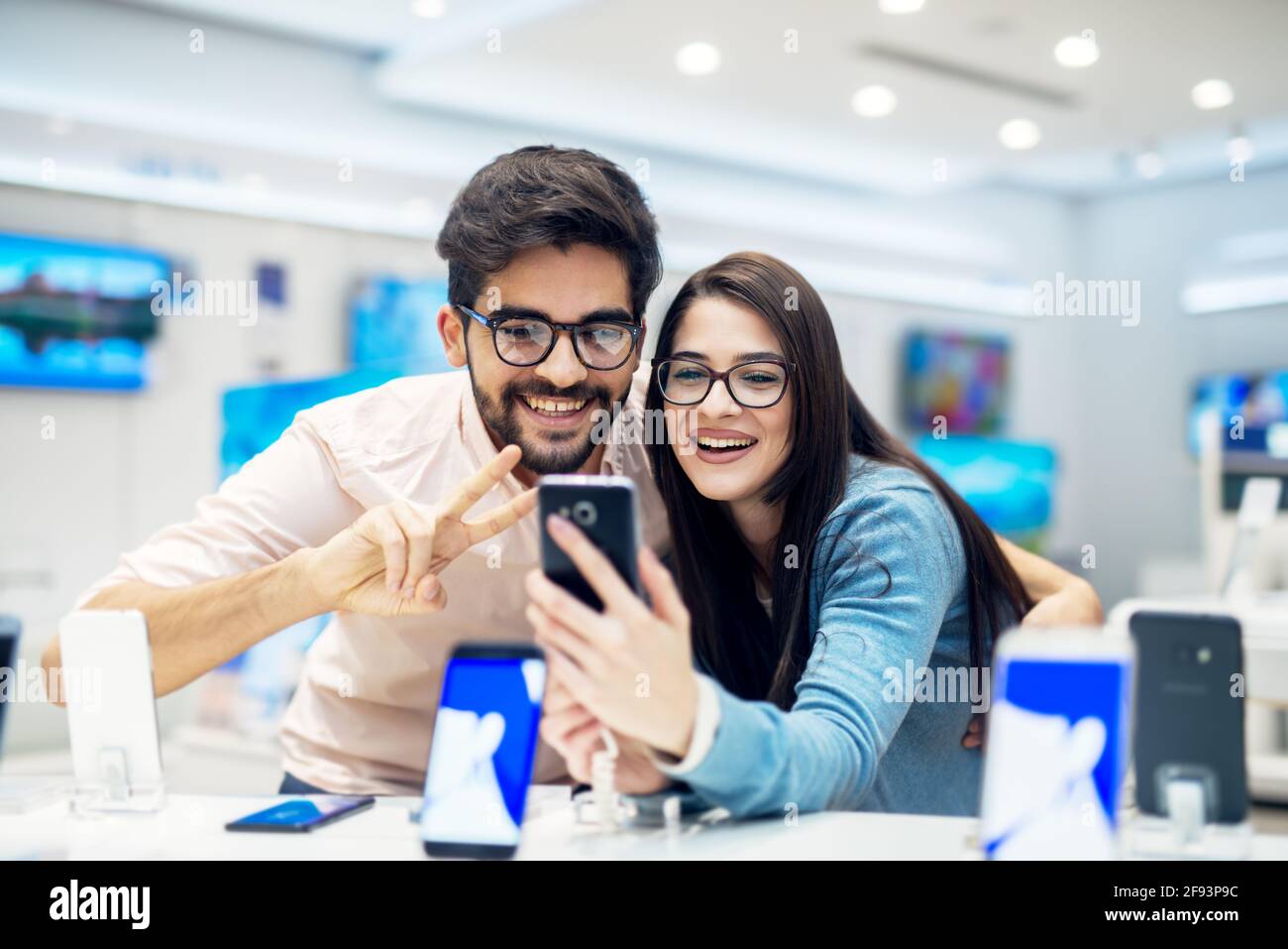 Giovane soddisfatto elegante e affascinante coppia ha abbracciato la prova del nuovo modello di un mobile dalla scrivania nel negozio di tecnologia. Foto Stock