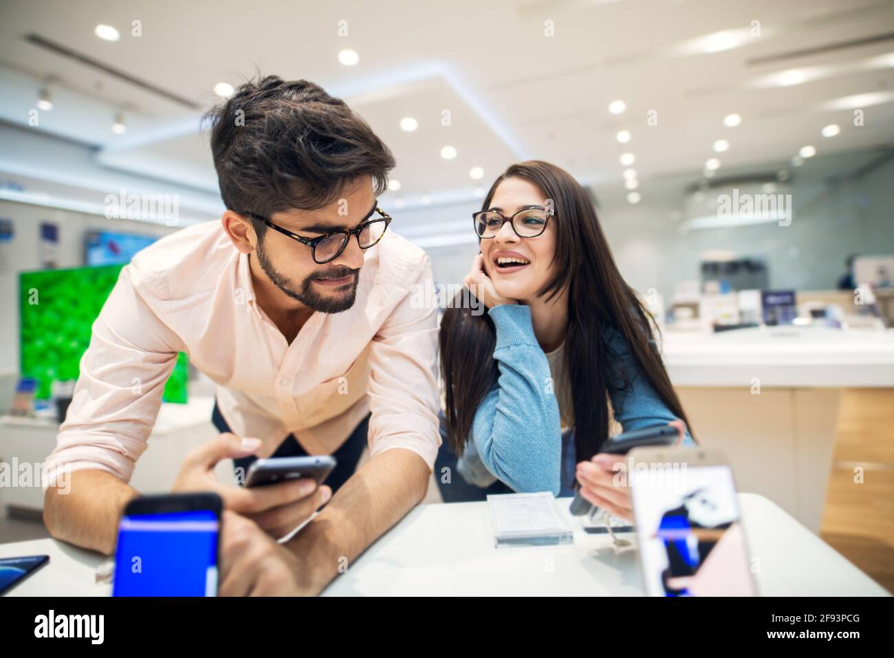 Giovane soddisfatto elegante coppia affascinante testare il nuovo modello di un mobile dalla scrivania nel negozio di tecnologia. Foto Stock