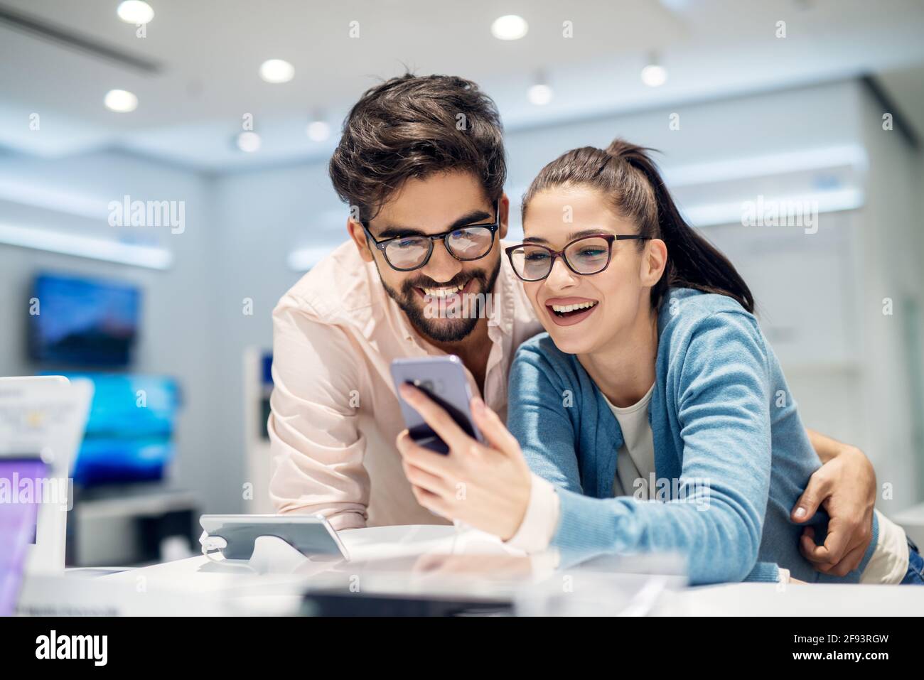 Giovane soddisfatto elegante coppia affascinante testare il nuovo modello di un mobile dalla scrivania nel negozio di tecnologia. Foto Stock