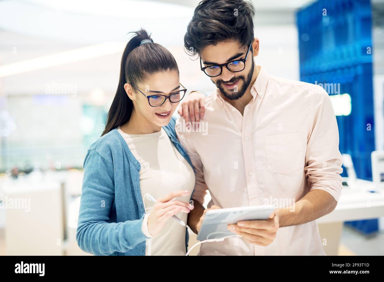 Giovane hipster elegante coppia sorridente multirazziale testare il nuovo modello di un tablet con una matita nel negozio di tecnologia. Foto Stock