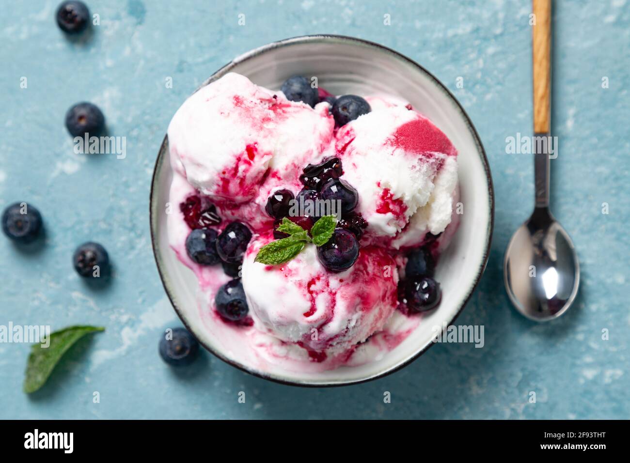 Yogurt fatto in casa e gelato al mirtillo con sciroppo di mirtillo naturale in una ciotola su fondo blu ruvido. Vista dall'alto Foto Stock