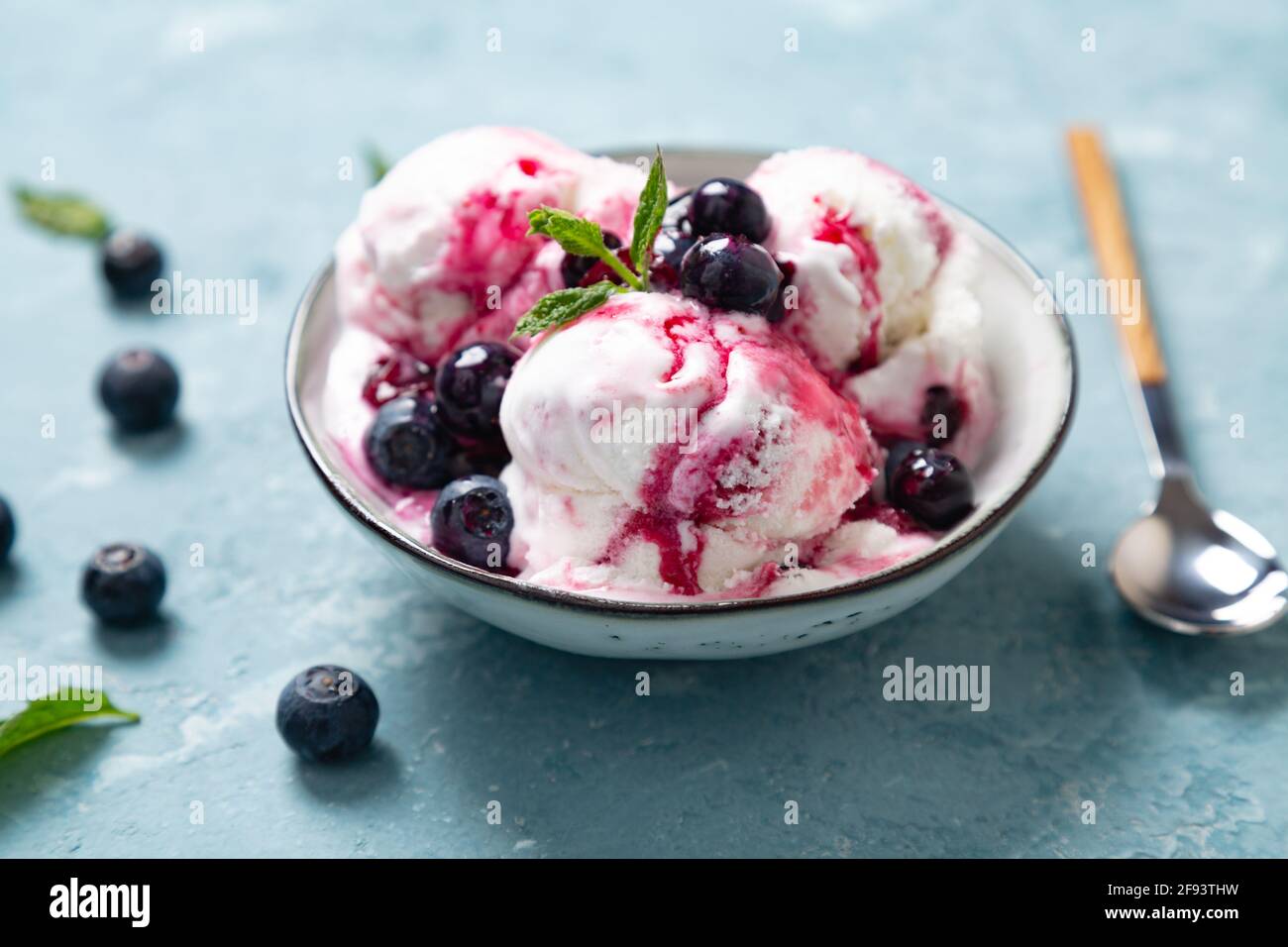 Yogurt fatto in casa e gelato al mirtillo con sciroppo di mirtillo naturale in una ciotola su sfondo blu ruvido Foto Stock