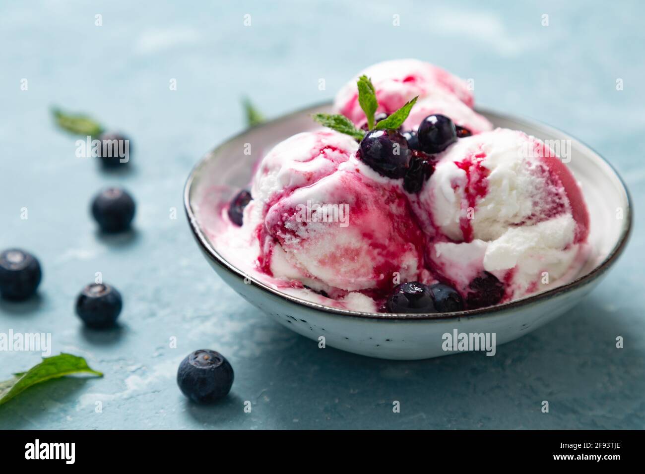 Yogurt fatto in casa e gelato al mirtillo con sciroppo di mirtillo naturale in una ciotola su sfondo blu ruvido Foto Stock